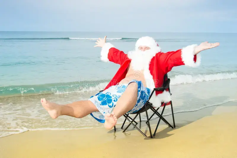 Santa relaxing on the beach, arms outstretched, wearing swim trunks, ocean background.
