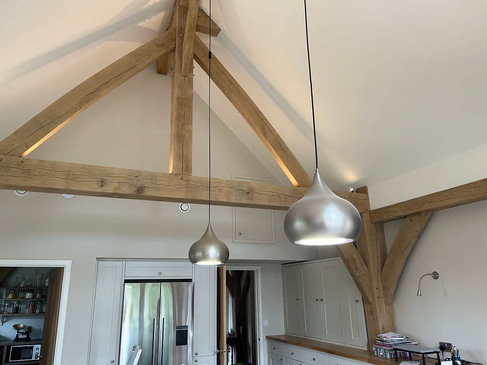 Wooden beams and metallic pendant lights in a modern kitchen with white cabinets and a silver fridge. Bright, open space with a warm feel.