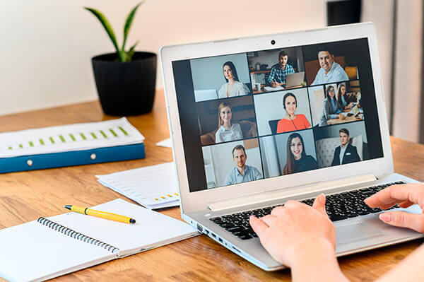 An individual takes part in an online live lecture, with multiple students appearing on a laptop screen