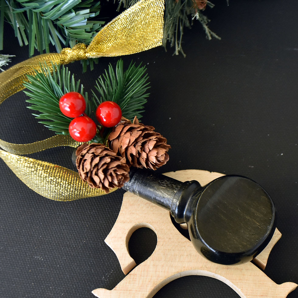Handmade dark wood cello tuning peg Christmas ornament accented with holly berry and pinecone greenery, hanging from a sparkl