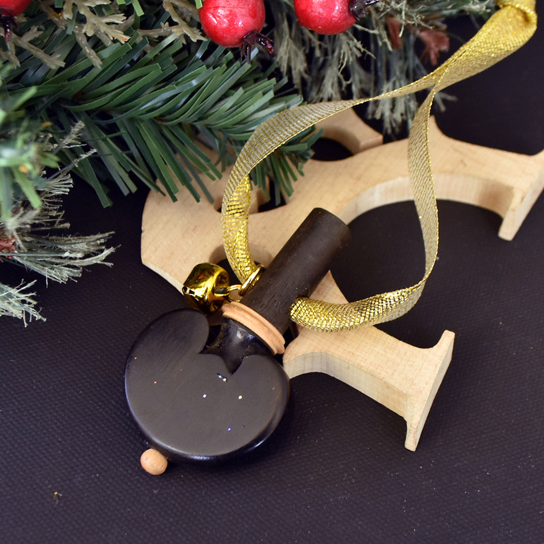 Handmade dark wood cello tuning peg Christmas ornament with light wood accents and gold jingle bell, hanging from a glittery