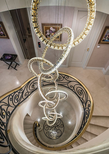 Grand spiral staircase with elegant modern chandelier hanging down its center.