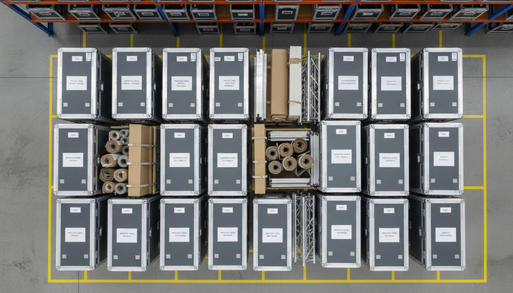 Bird's-eye view of stacked transport crates with labeled exhibition stand modules.
