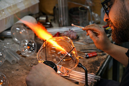 Artisan shaping molten glass with a torch in a glassblowing workshop.