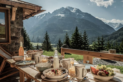 Outdoor dining table with breakfast and mountain backdrop at Benglerwald Berg Chalets