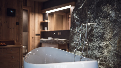 Freestanding bathtub beside natural stone wall in a chalet with private spa