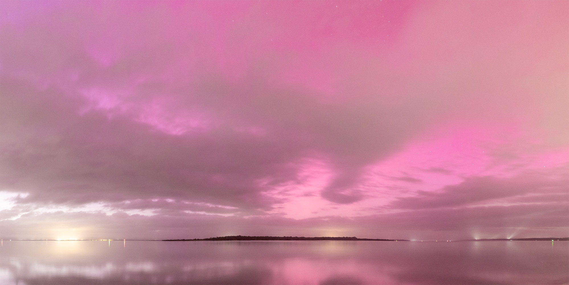 A pink morning scene across the Peel Harvey Estuary with the light of sunrise to the left, clouds cover some of the sky giving it depth. The water is soft and still