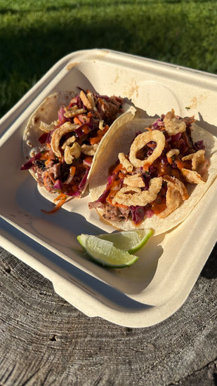 Two delicious pork tacos with crispy onion toppings, citrus slaw, lime, in a container outdoors.