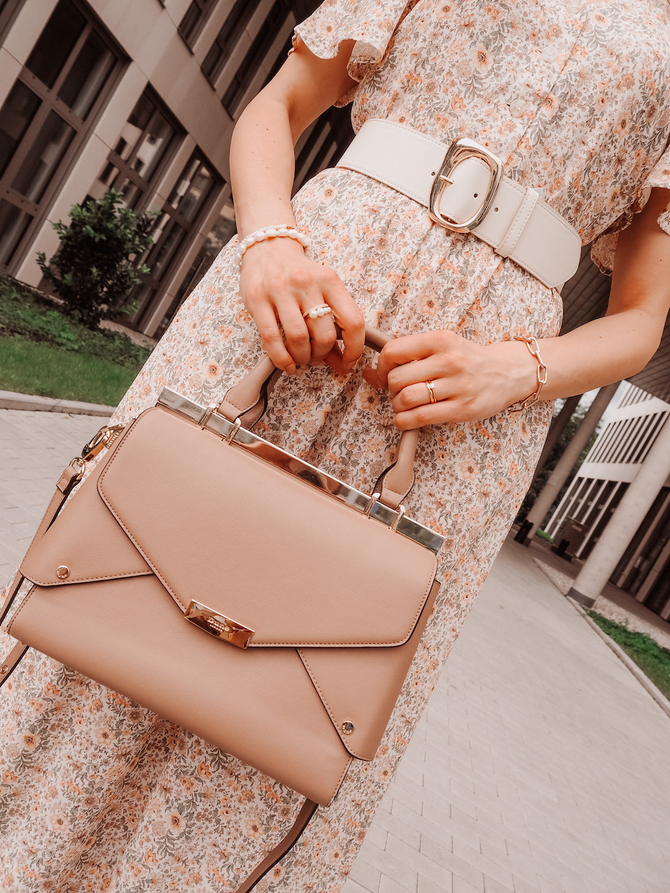 Nahaufnahme von Outfit-Details mit brauner Tasche und hellem Blumenkleid sowie Taillengürtel und Perlenschmuck