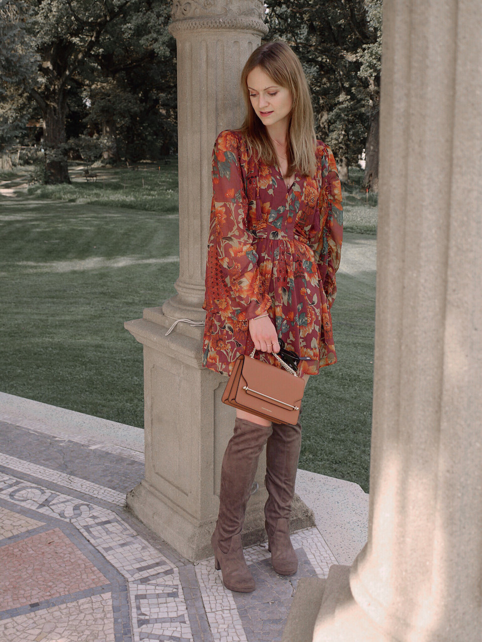 Autumn Outfit. Girl dressed in dark floral dress, over the knee boots carrying a tan bag