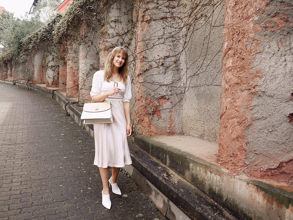 Girl dressed in lace blouse, satin skirt, white mules, and Coach Parker bag