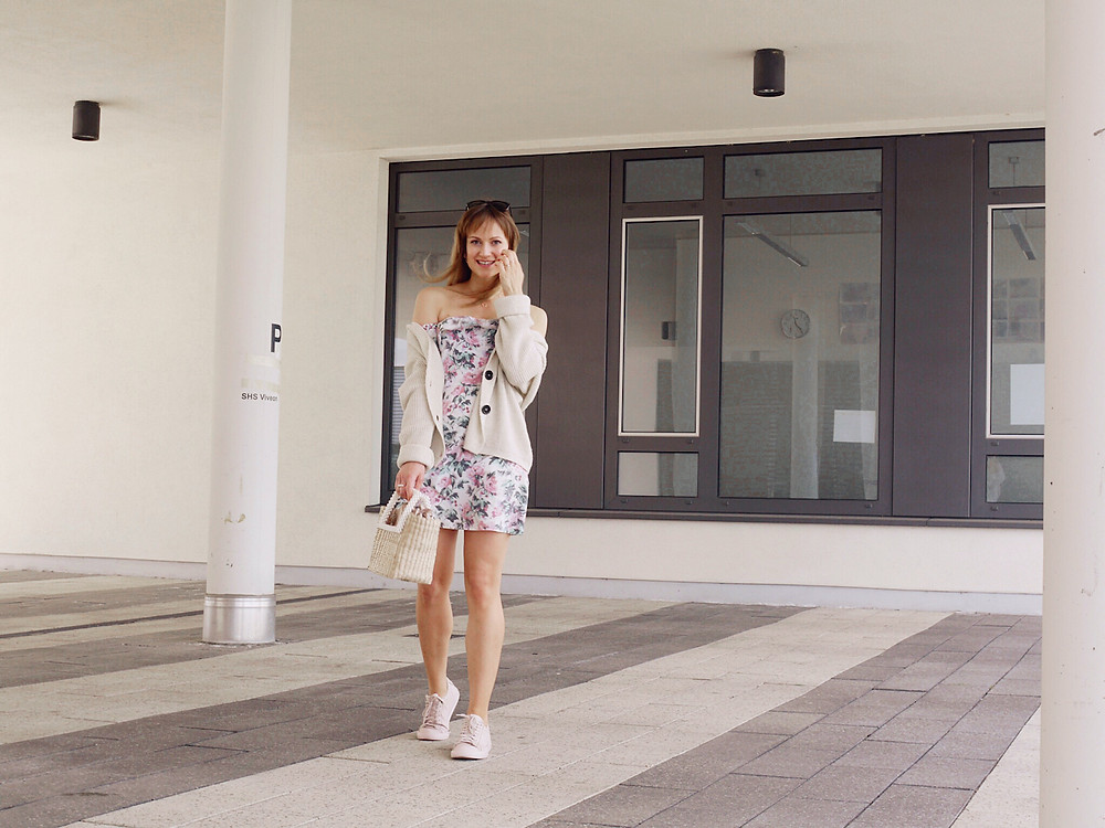 Girl dressed in floral summer dress, cardigan, pink sneakers and basket bag