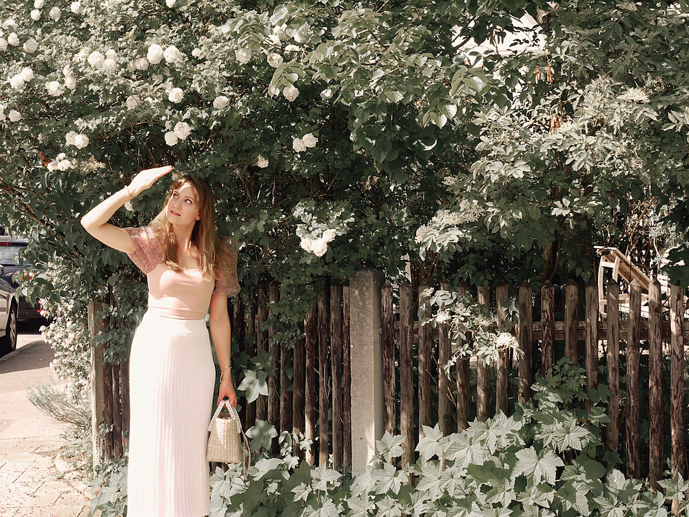 Girl wearing a cream midi skirt, puff sleeve floral top, straw bag, and heeled sandals