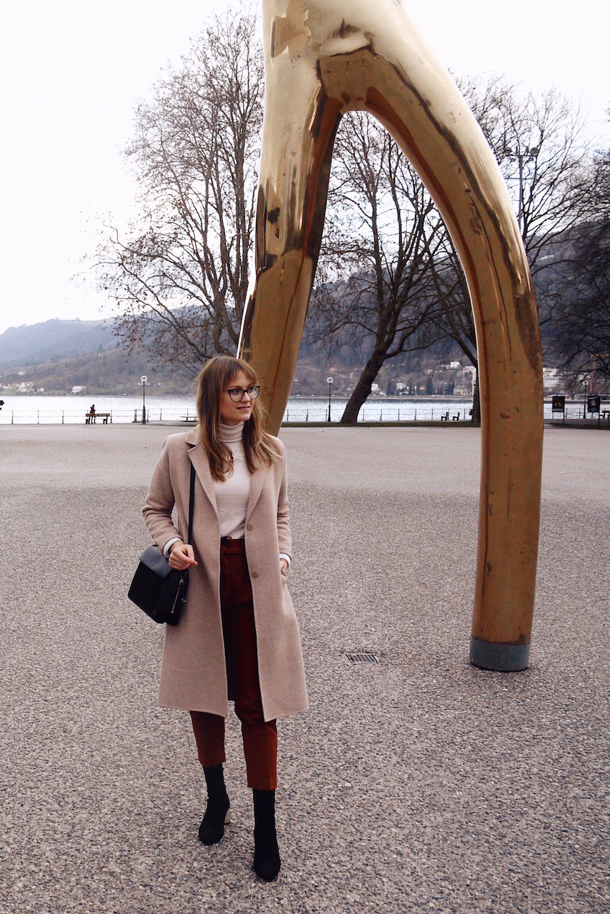 Girl in office outfit consisting of paperbag pants, roll neck jumper and white blazer standing between golden bars