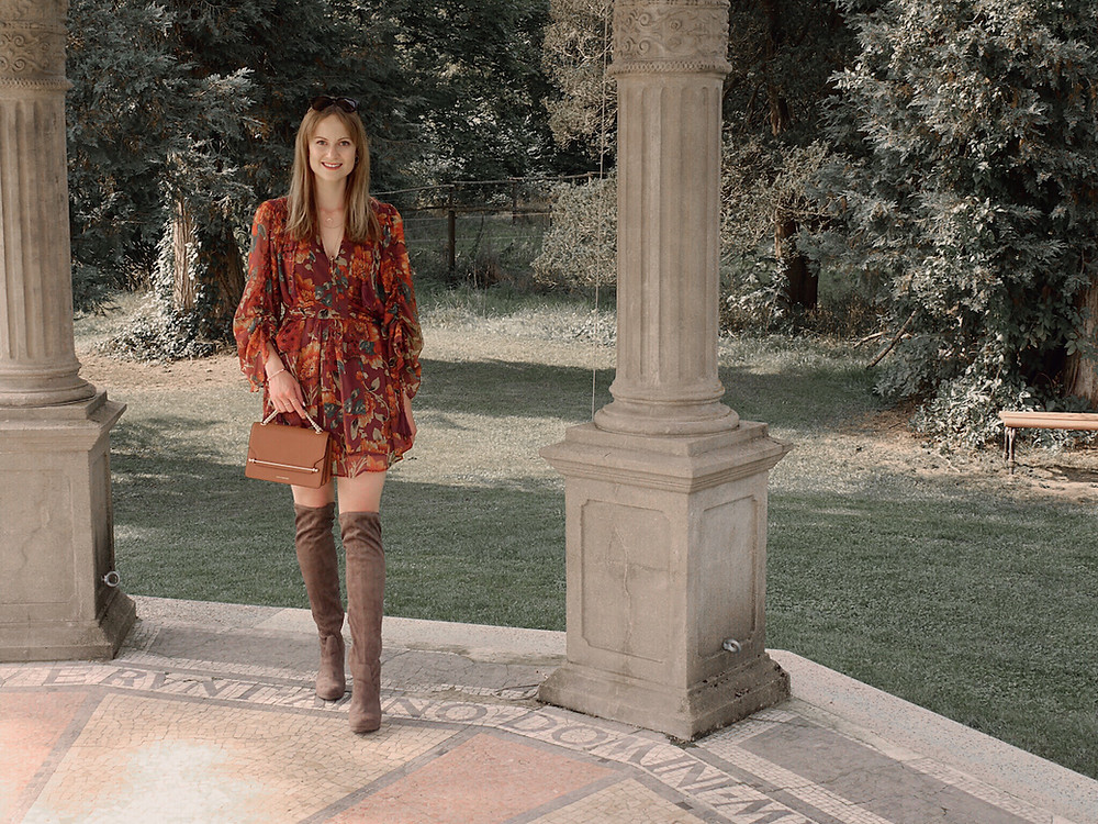 Autumn Outfit. Girl dressed in dark floral dress, over the knee boots carrying a tan bag