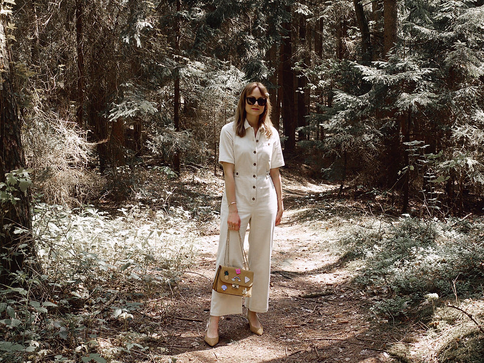 Girl wearing an outfit consisting of a white boilersuit, yellow bag and suede heels standing in the forest