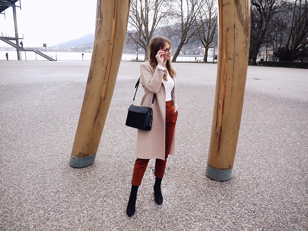Girl in office outfit consisting of paperbag pants, roll neck jumper and white blazer standing between golden bars