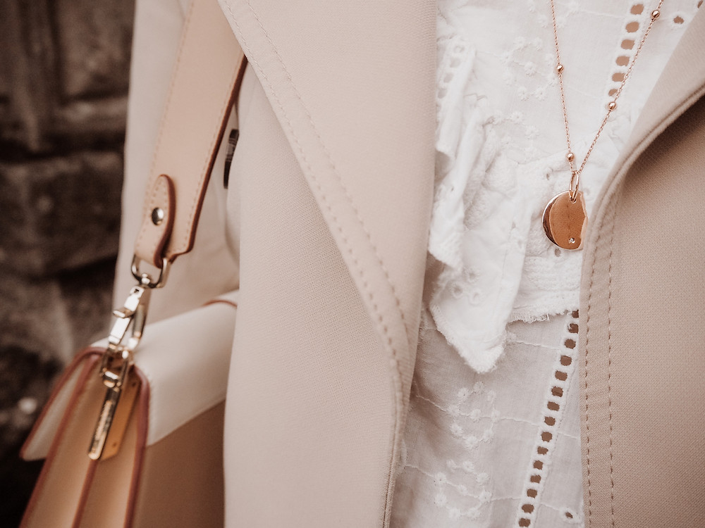 Outfit detail shot with a trench coat, white lace blouse and Strathberry bag