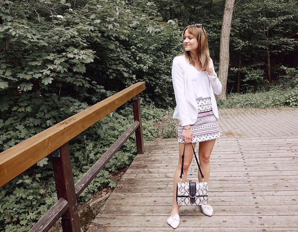 Girl in a white outfit with t-shirt, blazer and patterned skirt, holding an animal print bag, on a bridge