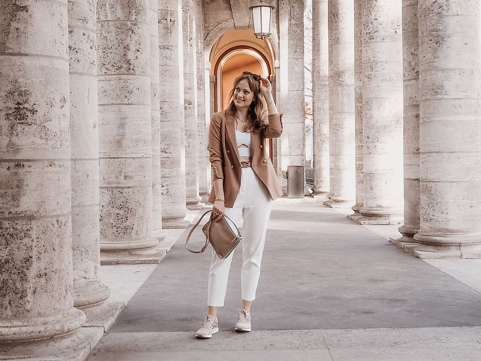 Young woman dressed in a beige blazer, white trousers and a white bralette, with a beige handbag and sneakers in an arcade