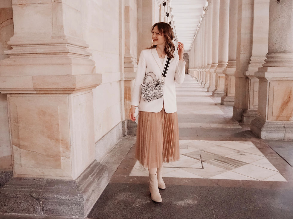 Young woman dressed in a blazer and tulle skirt with beige boots standing in a corridor of columns