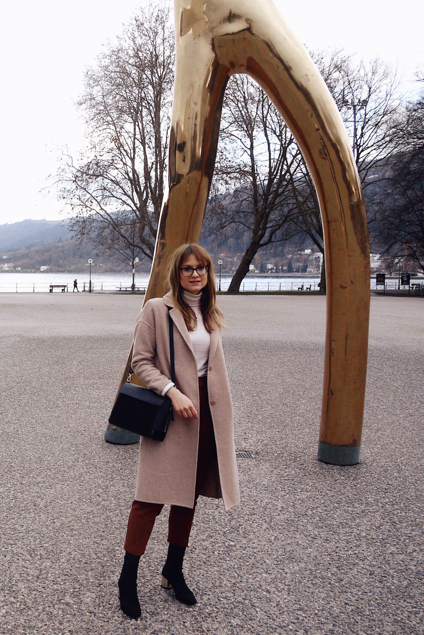 Girl in office outfit consisting of paperbag pants, roll neck jumper and white blazer standing between golden bars