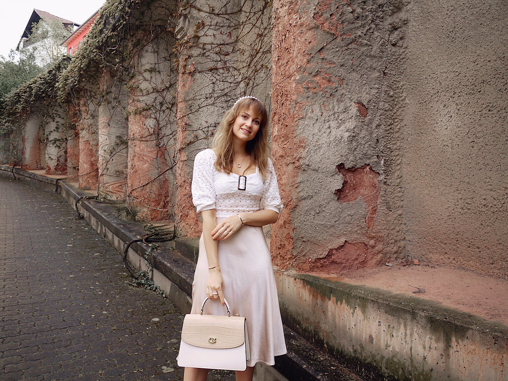 Girl dressed in lace blouse, satin skirt, white mules, and Coach Parker bag