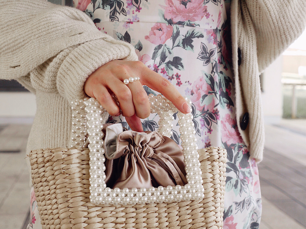 Junge Frau in geblümtem Sommerkleid, Strickjacke, rosa Sneakern und Korbtasche
