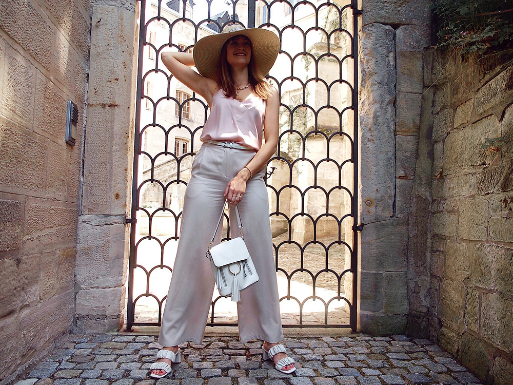 Young woman dressed in a light pink lingerie top, beige linen shorts, white sandals and big straw hat