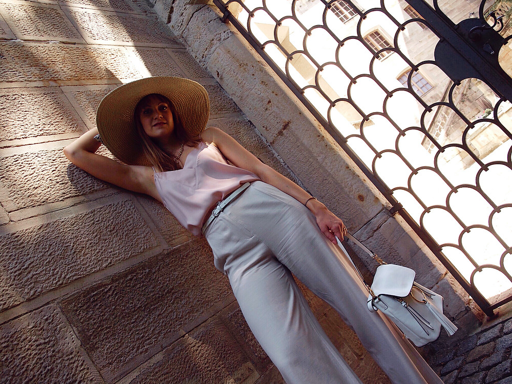 Young woman dressed in a light pink lingerie top, beige linen shorts, white sandals and big straw hat
