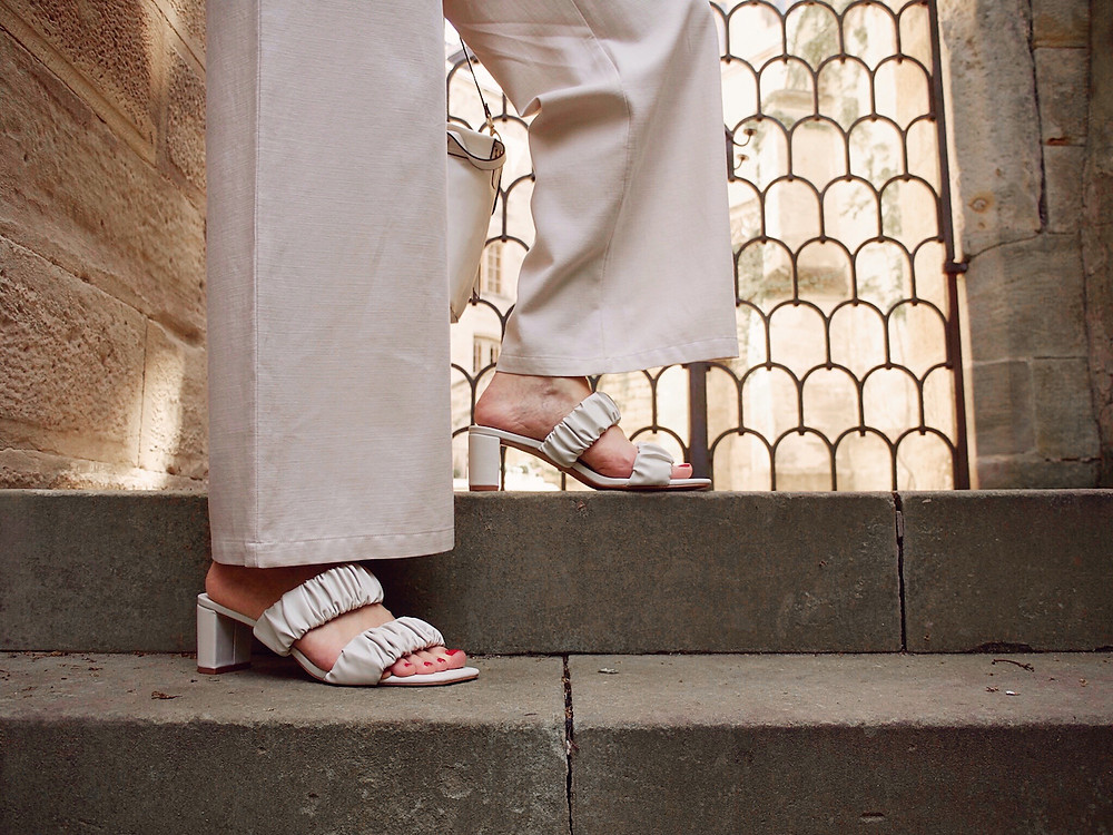 Closeup of white sandals worn with beige trousers