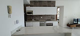 Modern kitchen interior at Menesse 32 in Playa del Carmen, featuring white marble breakfast bar, full-size electric appliances including oven, stove, dishwasher, microwave, and refrigerator. Sleek white cabinetry, dark tiled backsplash, and open layout connected to living room and bedroom area.