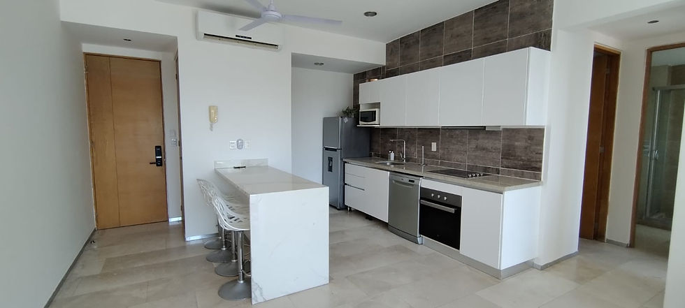 Entrance and integrated kitchen of Playa del Carmen condo featuring a sleek marble breakfast island with bar stools, high-end electric appliances including a dishwasher, oven and refrigerator, overhead microwave, modern tile backsplash, and split-unit A/C with ceiling fan for climate control.