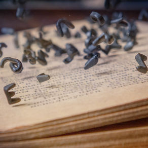 Letras metálicas suspendidas sobre las páginas de un libro antiguo, representando el poder de la escritura y la preservación del conocimiento.