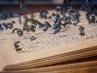 Letras metálicas suspendidas sobre las páginas de un libro antiguo, representando el poder de la escritura y la preservación del conocimiento.