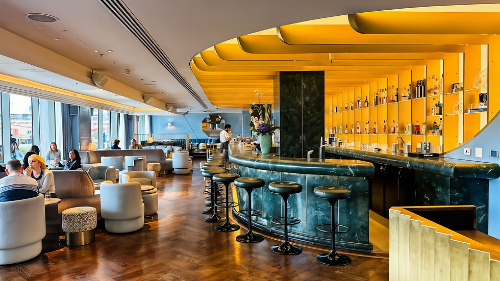 Stylish bar with green counter, yellow ceiling, and shelves of bottles. People seated on gray chairs, engaged in conversation. Relaxed mood.