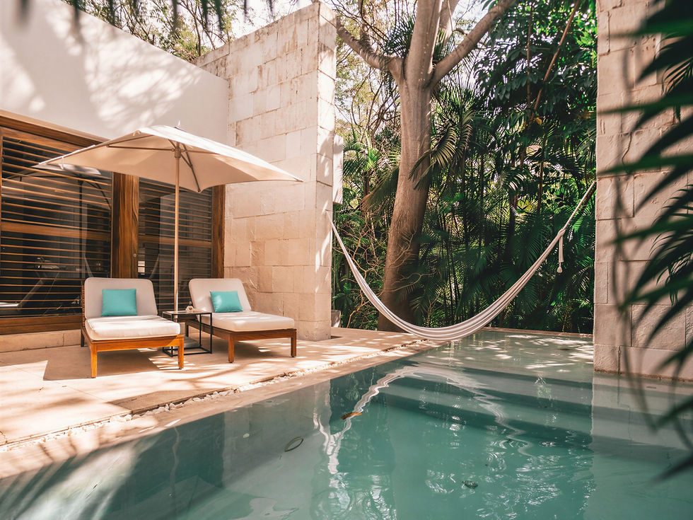 Poolside scene with lounge chairs under an umbrella, a hammock between trees, and a serene blue pool. Surrounded by lush greenery.