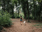 A woman and her dog walk on a wooded trail.