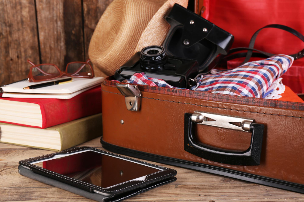 A packed suitcase sits opened with a hat, camera, and e-reader nearby.