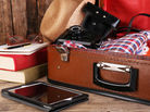 A packed suitcase sits opened with a hat, camera, and e-reader nearby.