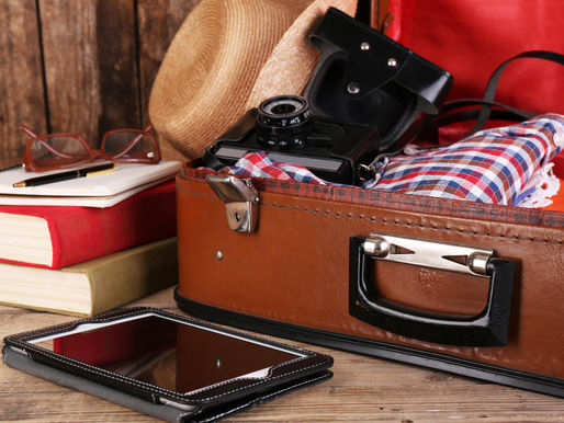 A packed suitcase sits opened with a hat, camera, and e-reader nearby.