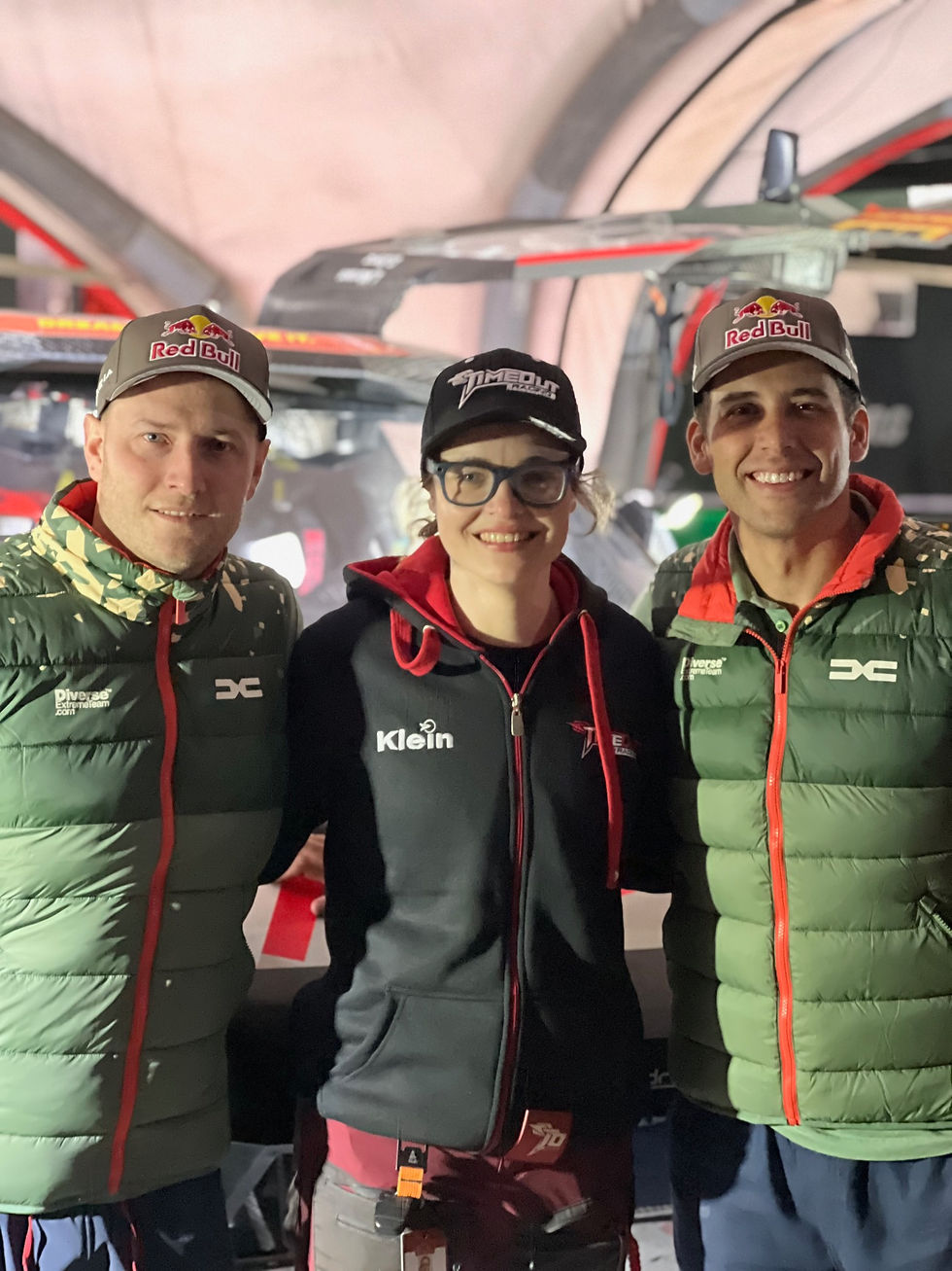 Three smiling race team members in Red Bull caps pose indoors before a rally car, with Klein and Timeout Racing logos visible.