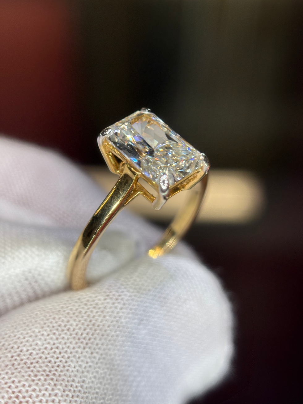 Thumbnail: Emerald cut diamond ring on a gold band held in a gloved hand