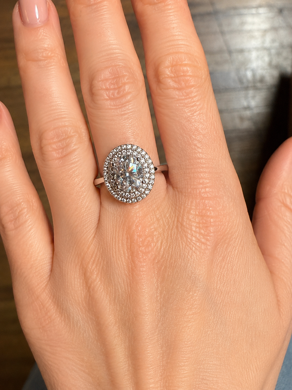 Sterling silver ring with a round lab-created moissanite center stone and an oval double halo, worn on a hand