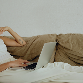 Une femme allongée sur son canapé avec un ordinateur sur le genou pour faire une téléconsultation diététique