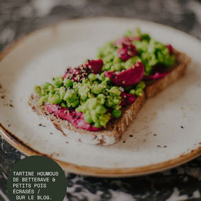 Tartine de pain garnie de houmous de betterave et de petits pois écrasés, parsemée de graines, sur une assiette en céramique.