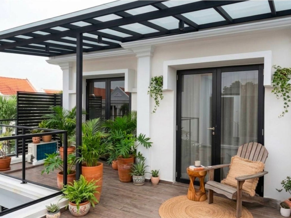 Modern balcony with wooden decking, potted tropical plants, timber lounge chair, black-framed canopy and glass doors.
