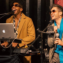 Dúo musical de Jimmy & The Benjamins interpretando en vivo: vocalista con micrófono y tecladista con laptop, ambientando un evento con energía y estilo.