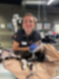 A veterinary nurse in scrubs smiles at the camera standing over a cat receiving oxygen.