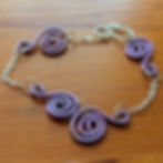Fine silver chain bracelet with four purple wire swirl pendants. Shown on wooden surface.